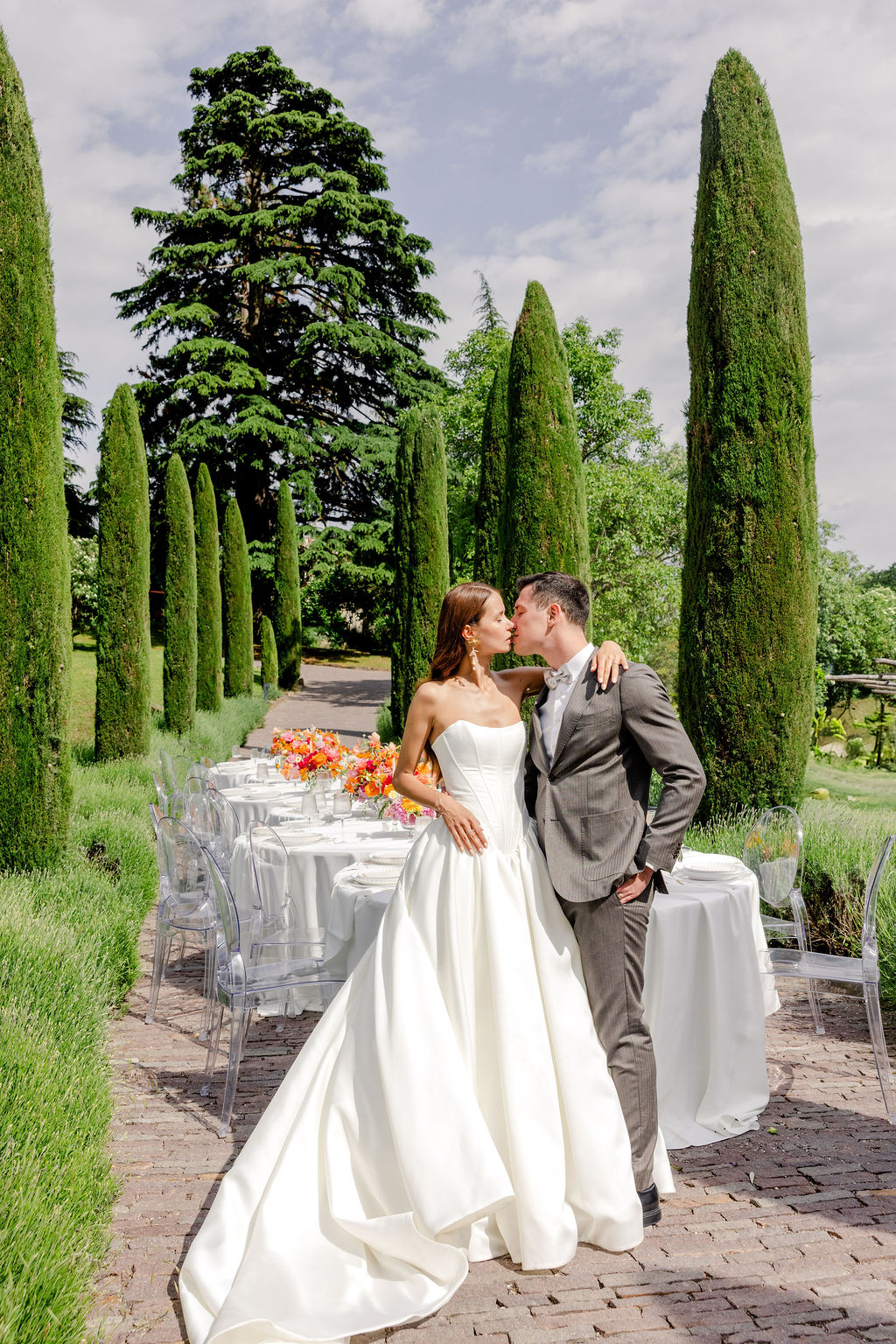 Bei einer exklusiven Hochzeit am Comer See küssen sich Braut und Bräutigam neben einem langen Esstisch im Freien.