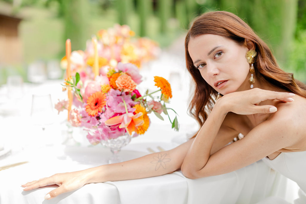 Eine Frau sitzt bei einer exklusiven Hochzeit in der Toskana an einem Tisch mit farbenfrohen Blumenarrangements.