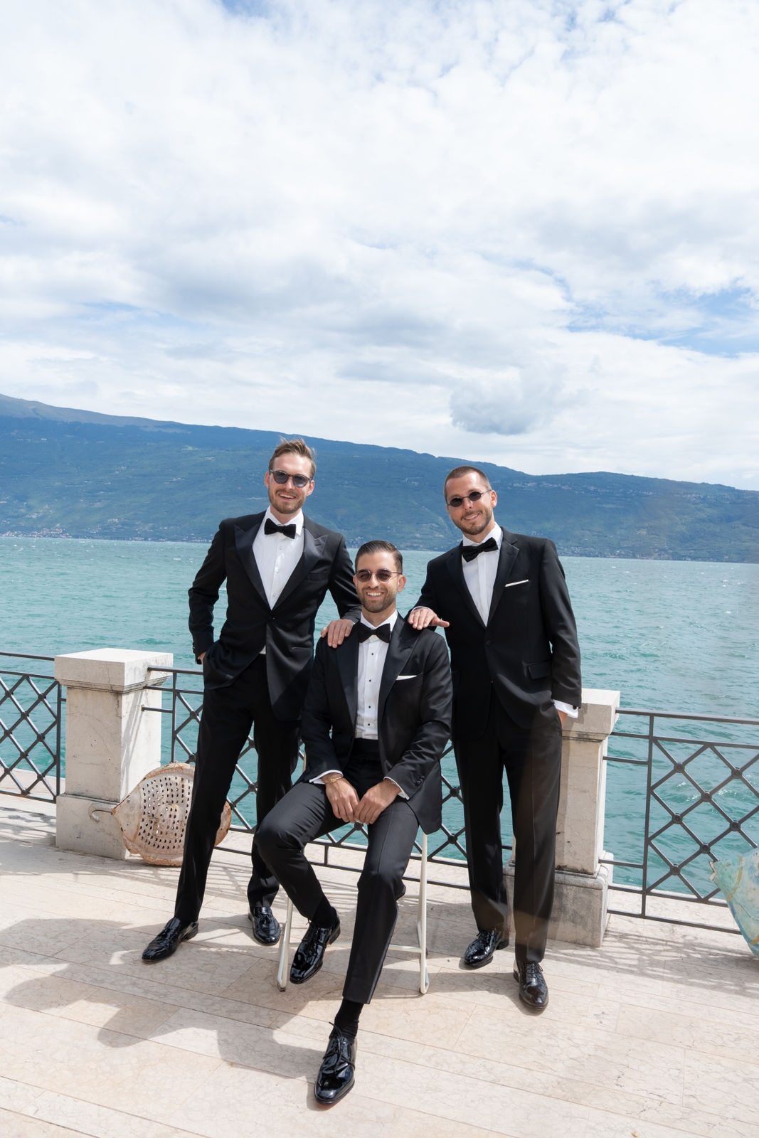 Drei Männer in schwarzen Smokings auf einer Terrasse mit Blick auf einen See – ideal für exklusive Veranstaltungen.