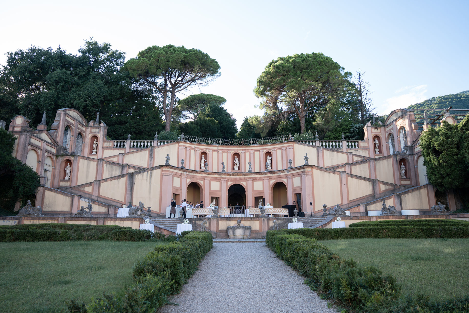 Ein Kiesweg führt zu einer kunstvoll gestalteten Terrasse einer italienischen Villa am Comer See, die von gepflegten Hecken eingerahmt wird.