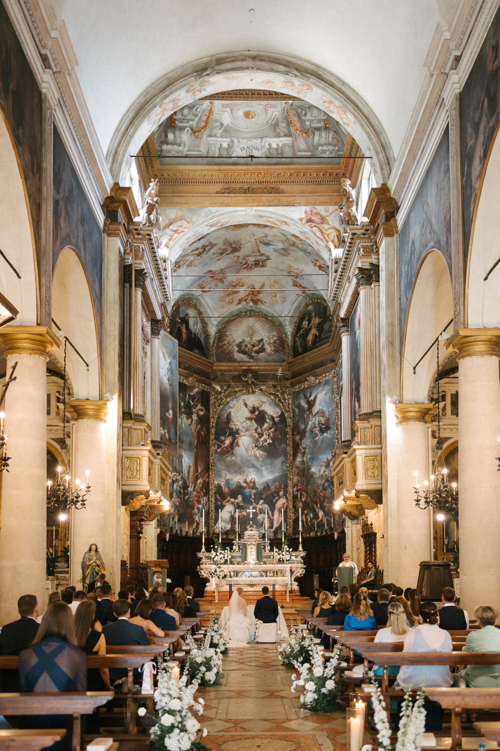 Bei einer exklusiven Hochzeit in einer mit kunstvollen Gemälden geschmückten Kirche geben sich Braut und Bräutigam das Eheversprechen.