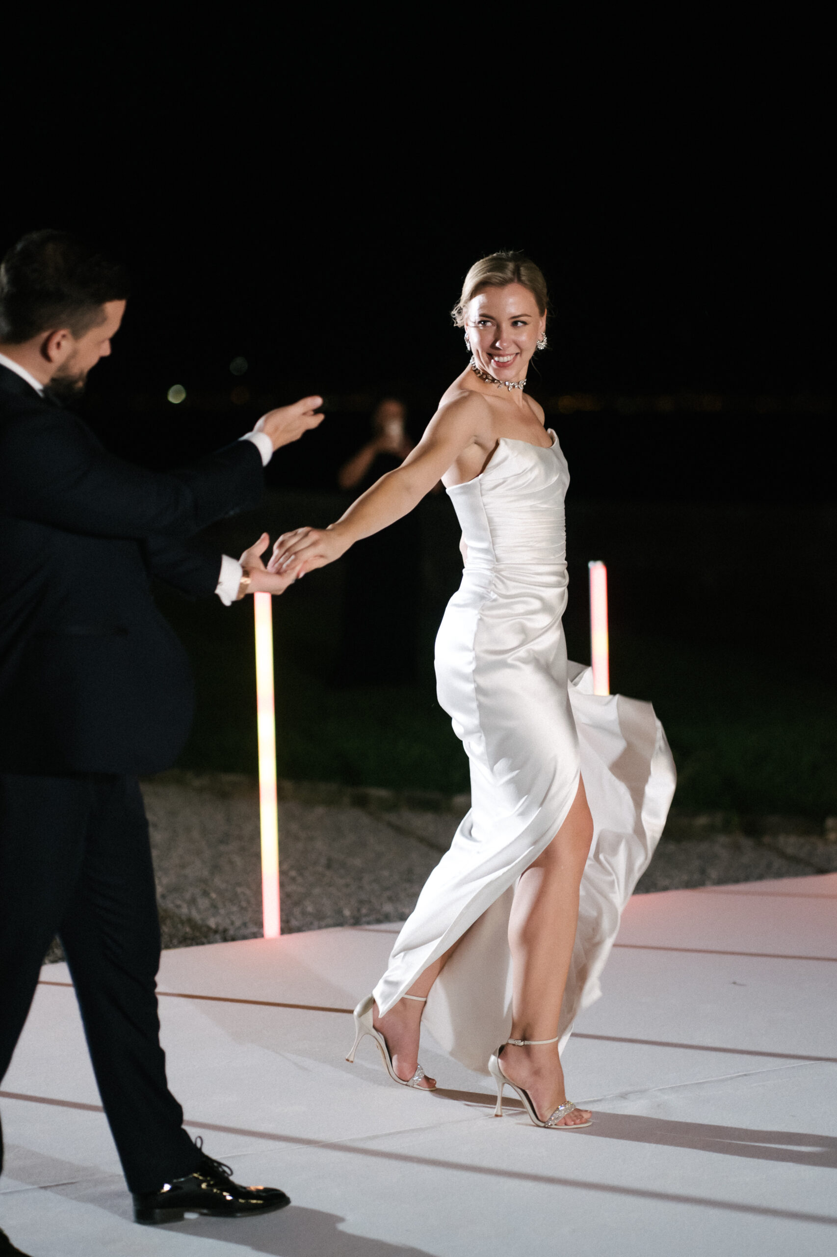 Ein Brautpaar, das nachts auf einer beleuchteten Bühne zu seiner exklusiven Hochzeit tanzt.