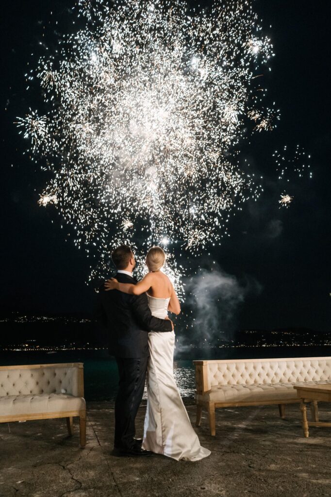 Brautpaar blickt Arm in Arm auf ein Feuerwerk über dem See – ein magischer Moment einer Luxushochzeit in Italien.